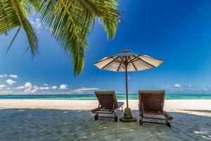 schöne tropische sonnige küste, paar sonnenliegen stühle regenschirm unter palmenblättern. Meer Sand Horizont Himmel. romantischer Relax-Lifestyle inspiriert den Hintergrund des Inselstrandes. sommerreise exotischer urlaub foto