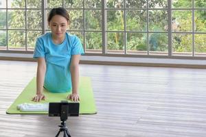 junge asiatische frau konzentriert sich auf das üben der yoga-kobra-pose und folgt dem online-tutorial vom smartphone zu hause. junge menschen häusliches lebenskonzept. selektiver fokus und kopierraum. foto