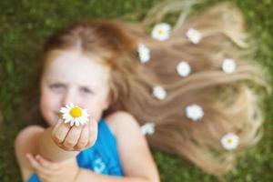 Porträt eines schönen kleinen Mädchens mit gesunden roten Haaren mit Kamillenblüten, die auf dem Gras liegen foto