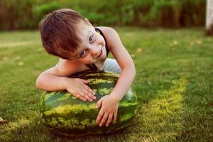 Porträt eines glücklichen Jungen mit einer großen ganzen Wassermelone im Hinterhof foto