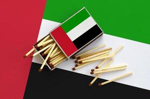 die flagge der vereinigten arabischen emirate wird auf einer offenen streichholzschachtel gezeigt, aus der mehrere streichhölzer fallen und auf einer großen fahne liegt foto