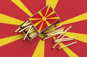 Die Mazedonien-Flagge wird auf einer offenen Streichholzschachtel gezeigt, aus der mehrere Streichhölzer fallen und auf einer großen Flagge liegt foto