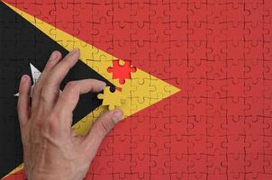 die flagge von timor leste ist auf einem puzzle dargestellt, das die hand des mannes zum falten vervollständigt foto