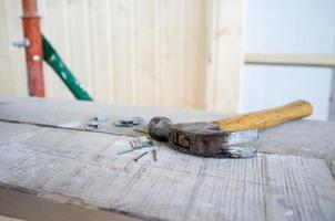 hammer und nägel liegen auf dem gerüst, vor dem hintergrund einer wand aus holzlatten. Arbeitsprozess. Hausrenovierung. foto