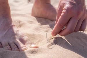 Ein barfüßiger Mann ging am Strand entlang und fand eine Glasscherbe einer Flasche, die gefährlich im Sand lag. foto