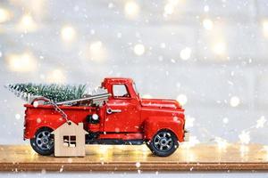 Rotes Retro-Auto mit einem Weihnachtsbaum schmückt mit dem Hausschlüssel im Pickup-Truck zu Weihnachten. Hauskauf, Umzug, Hypothek, Darlehen, Immobilien, Feststimmung, Neujahr foto