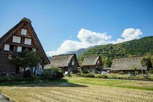 japanisches shirakawago-dorf im oktober in der herbstherbstlaubsaison. shirakawa traditionelles haus auf dreieckdach mit einem hintergrund von reisfeld, kiefernberg und klarem wolkenhimmel danach. foto