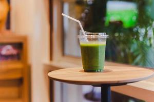 Grüner Smoothie in Plastikglas mit Strohhalm auf Holztisch im Café. foto