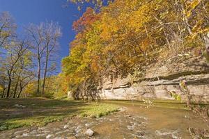 Herbstfarben und eine Kalksteinklippe über einem ruhigen Bach. foto