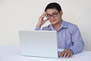 asiatischer büroangestellter mittleren alters fühlt heachache, sieht ernst aus, denkt nach und plant etwas während der arbeit am laptop-computer. konzept, gesundheitliche probleme, arbeit mit daten. foto