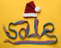 inschrift verkauf von einem schal und einer mütze des weihnachtsmanns oben auf gelbem hintergrund. konzept der neujahrsrabatte und einkäufe. foto