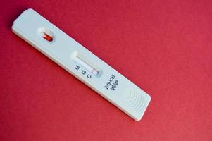 test auf coronavirus liegt auf rotem hintergrund. weißer Teststreifen auf hellem Hintergrund zur Bestimmung der Infektion. sensitiver Test auf Coronavirus-Antikörper foto