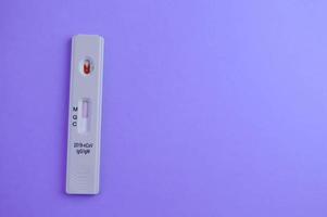 Der Test auf Coronavirus liegt auf einem violetten Hintergrund. ein Tropfen venöses Blut auf dem Teststreifen. medizinisches labor, express-diagnostik von coronavirus foto