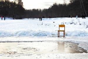 eisgebundener Stuhl in der Nähe von Öffnungswasser in einem zugefrorenen See foto