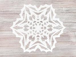 Schneeflocke aus Papier geschnitzt auf hellbraunem Brett foto