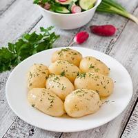 Junge gekochte Kartoffeln mit Butter und Dill auf einem weißen Teller foto