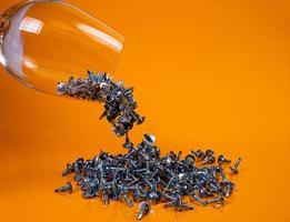 ließ viele selbstschneidende Metallschrauben aus Stahl in ein Glas fallen, in ein Eimerglas. selbstschneidende Schraube für Metall, für Eisen, verchromte selbstschneidende Schraube, auf orangegelbem Hintergrund, foto