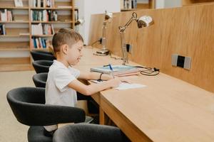 der junge sitzt in der bibliothek und schreibt am tisch in ein notizbuch. Hausaufgaben vorbereiten. ein guter Schüler. Schüler liebt es zu lernen. Freiraum in der Schule. foto