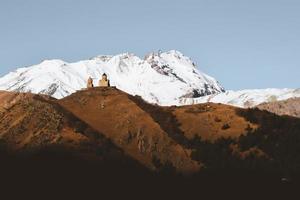 stepantsminda, gergeti, georgia. berühmte gergeti trinity tsminda sameba kirche in früher winterlandschaft. Geländewagen, der sich im frühen Winter in der Nähe einer Kirche in einer wunderschönen georgischen Landschaft bewegt foto