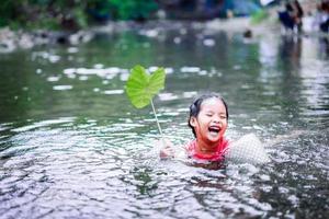 kleines asiatisches Mädchen, das im Wasser mit Lotusblatt spielt foto