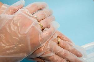 goldene Eheringe an den Händen in schützenden medizinischen Gummi-Einweghandschuhen zum Schutz vor gefährlichen tödlichen Krankheiten von Mikroben und Viren durch Coronavirus covid-19 auf blauem Hintergrund foto