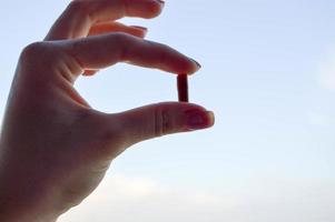 Eine braune, ovale Tablette wird in die Hände eines Mädchens mit Maniküre gedrückt. Frau hält Medizin auf einem Hintergrund von hellblauem Himmel. Hintergrund für medizinische Produkte foto