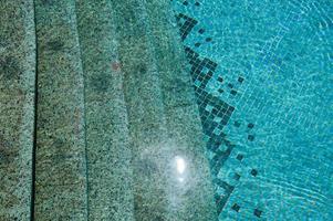 die Textur des Eingangs des Abstiegs in den Pool mit blauem Wasser und quadratischen Keramikfliesen auf den Stufen. der Hintergrund foto