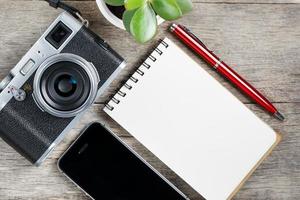 Klassische Kamera mit leerer Notizblockseite und rotem Stift auf grauem Holz, Vintage-Schreibtisch mit Telefon. foto