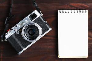 leere Notizblockseite und moderne Kamera im klassischen Stil auf dunkelbraunem Holztisch foto