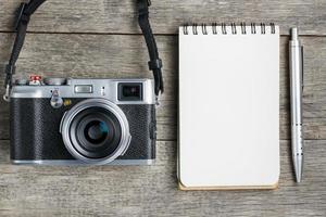 Klassische Kamera mit leerer Notizblockseite und grauem Stift auf grauem Holz, Vintage-Schreibtisch foto