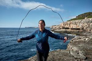 lateinische frau, mittleren alters, sportkleidung tragen, training, körperliche übungen machen, plank, sit-ups, kletterschritt, kalorien verbrennen, fit halten, draußen am meer, kopfhörer tragen, smartwatch foto