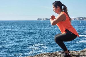 Fitness lateinamerikanische Frau im Sportset Training mit Gummiband, Gewichten, Gymnastikübungen, vor dem Wasser. foto