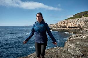 lateinische frau, mittleren alters, sportkleidung tragen, training, körperliche übungen machen, plank, sit-ups, kletterschritt, kalorien verbrennen, fit halten, draußen am meer, kopfhörer tragen, smartwatch foto