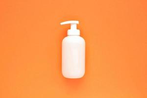 weiße, markenlose Plastikspender-Pumpflasche auf orangefarbenem Hintergrund mit Kopierraum für Text. kosmetikverpackungsmodell, flüssiger seifenflakon, händedesinfektionsmittel ohne etikett, shampoo bio spa, duschgel foto