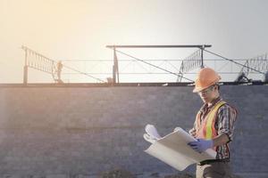 arbeiter mit sicherheitsweste und schutzhelm halten die blaue pause, die an der baustelle arbeitet, neues konstruktionsdesign und prüfungsprozess foto