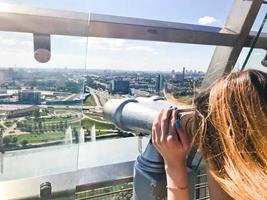 Ein schönes Mädchen betrachtet die Landschaft, ein Panorama der Stadt im Beobachtungsraum, ein Fernglas, ein Teleskop mit einem Geldscheinprüfer auf einer Aussichtsplattform im Freien foto