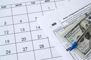 Formular 990 Rückkehr der Organisation von der Einkommenssteuer befreit und blauer Stift mit Dollarnoten liegt im Bürokalender. Steuerformular des Finanzamtes foto