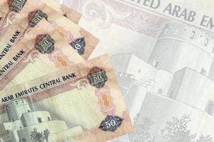 50 VAE-Dirham-Scheine liegen im Stapel auf dem Hintergrund einer großen halbtransparenten Banknote. abstrakter betriebswirtschaftlicher hintergrund foto