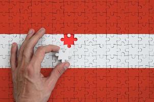 Die österreichische Flagge ist auf einem Puzzle abgebildet, das die Hand des Mannes zum Falten vervollständigt foto