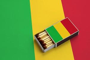 Die Mali-Flagge wird in einer offenen Streichholzschachtel gezeigt, die mit Streichhölzern gefüllt ist und auf einer großen Flagge liegt foto
