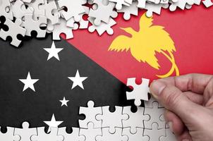 die flagge von papua-neuguinea ist auf einem tisch abgebildet, auf dem die menschliche hand ein weißes puzzle faltet foto