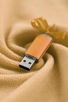 Eine orangefarbene USB-Flash-Speicherkarte mit Schleife liegt auf einer Decke aus weichem, pelzigem, hellorangefarbenem Fleece mit vielen Relieffalten. Speichergerät im Damendesign foto