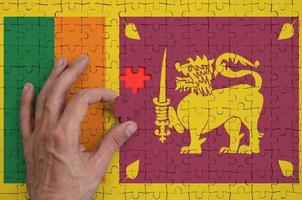 die flagge von sri lanka ist auf einem puzzle abgebildet, das die hand des mannes zu falten vervollständigt foto