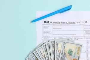 1041 Steuerformular liegt in der Nähe von Hundert-Dollar-Scheinen und blauem Stift auf hellblauem Hintergrund. US-Einkommensteuererklärung für Nachlässe und Trusts foto
