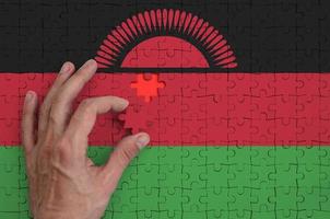 Die Malawi-Flagge ist auf einem Puzzle abgebildet, das die Hand des Mannes zum Falten vervollständigt foto