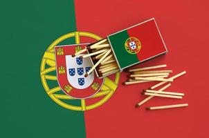 Die portugiesische Flagge wird auf einer offenen Streichholzschachtel gezeigt, aus der mehrere Streichhölzer fallen und auf einer großen Flagge liegt foto