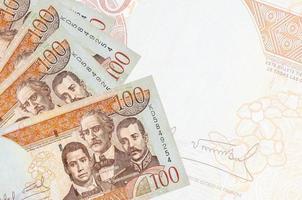 100 dominikanische Peso-Scheine liegen im Stapel auf dem Hintergrund einer großen halbtransparenten Banknote. abstrakter betriebswirtschaftlicher hintergrund foto