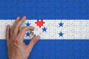 Die Flagge von Honduras ist auf einem Puzzle abgebildet, das die Hand des Mannes zum Falten vervollständigt foto