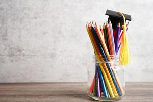 Abschlusshut mit bunten Bleistiften auf Buch mit Kopienraum, universitäres Bildungskonzept lernen.