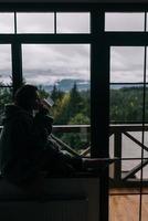 Silhouette einer Frau, die mit einem Becher auf der Fensterbank sitzt foto